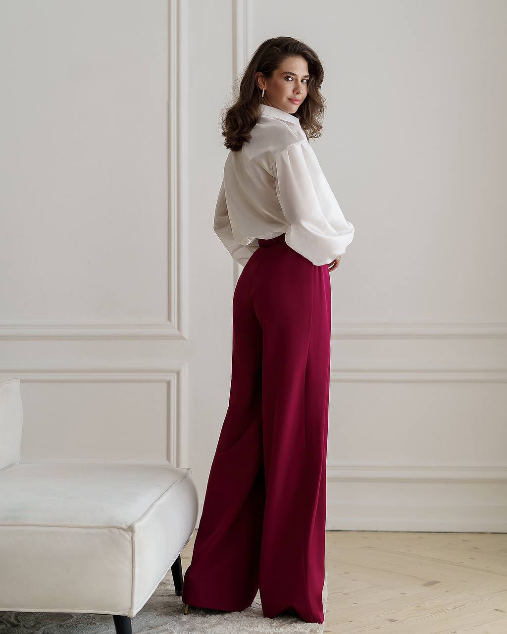 Woman wearing a white blouse and burgundy pants in an elegant room.