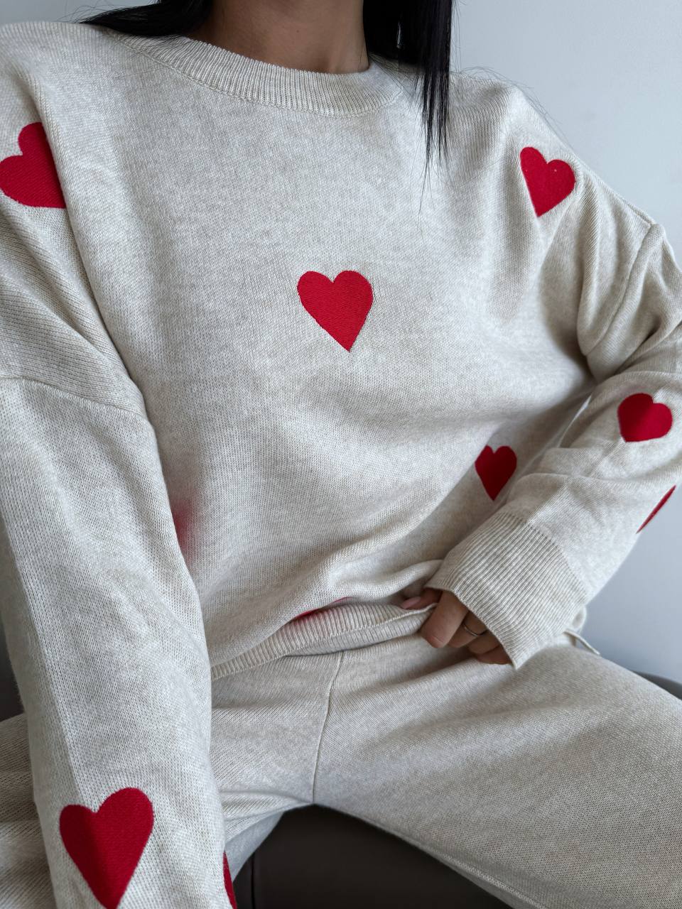 Person wearing a beige sweater with red hearts on a plain background