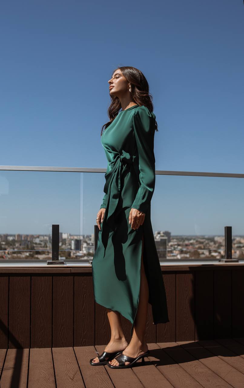 Woman in a green dress standing on a rooftop with a cityscape in the background