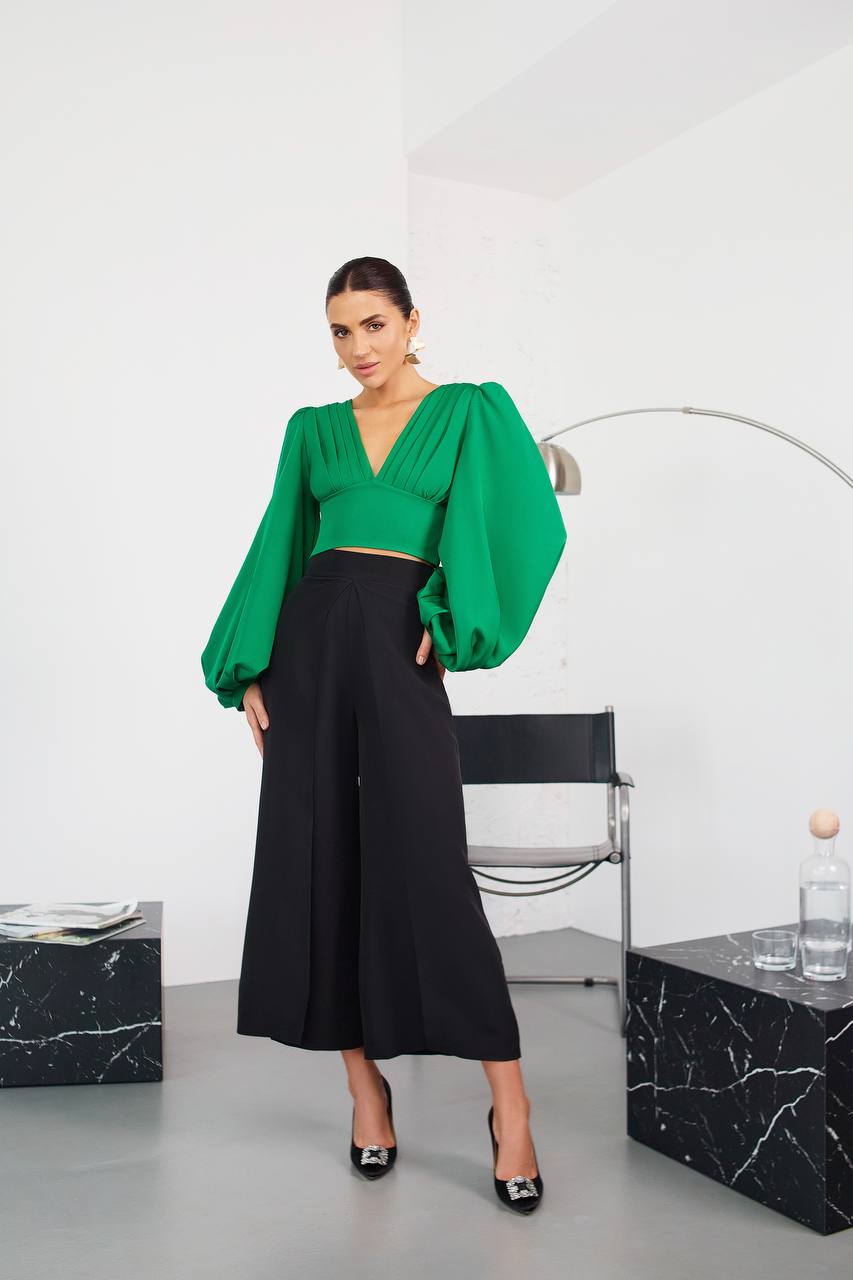 Woman wearing a green top and black pants in a modern interior setting