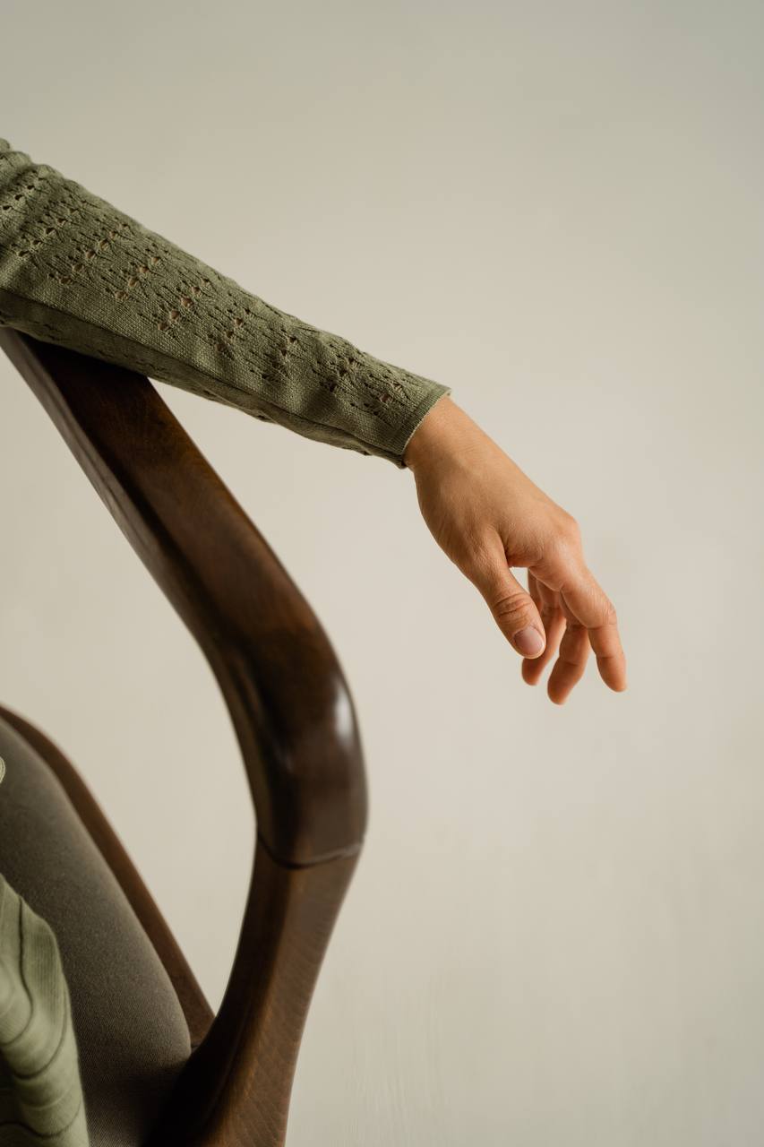 Person wearing a green sweater with lace detailing on a neutral background