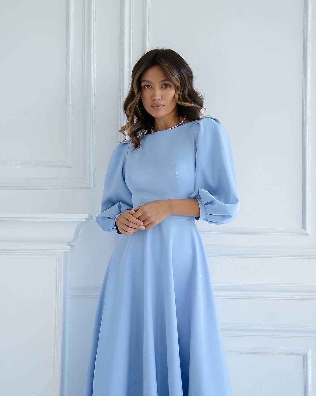Woman wearing a light blue dress against a white paneled wall