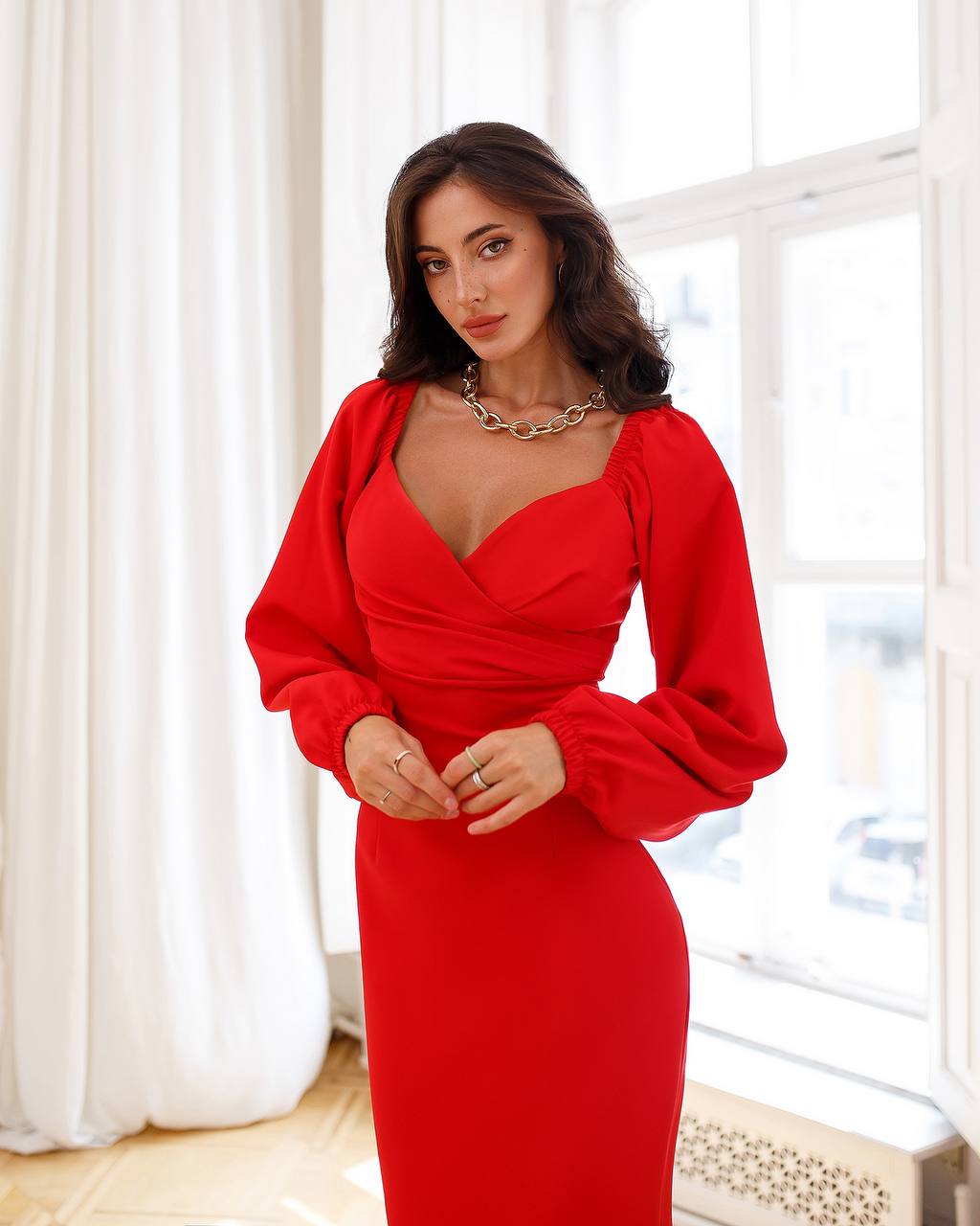 Woman wearing a red dress with long sleeves in a bright room.