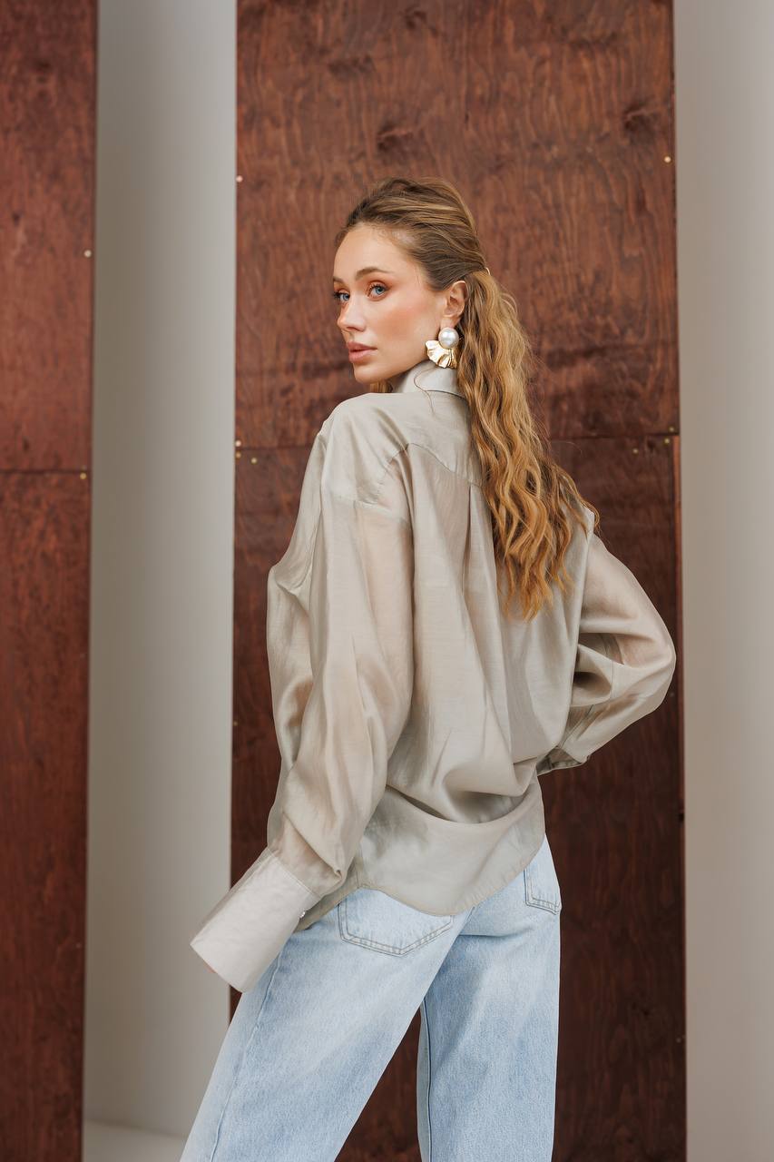Woman wearing a beige jacket and light blue jeans against a textured wall.