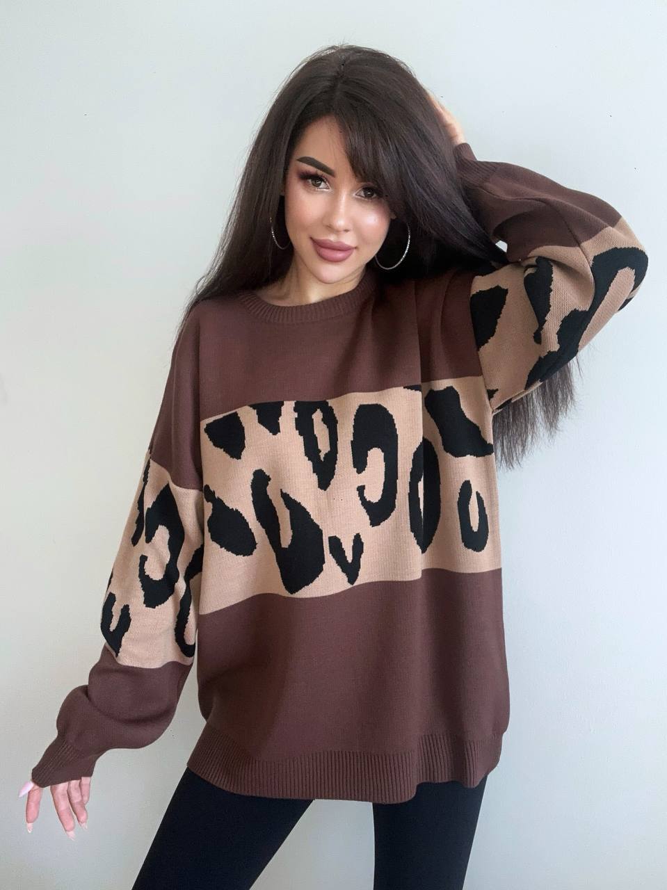 Woman wearing a brown sweater with leopard print pattern against a plain background