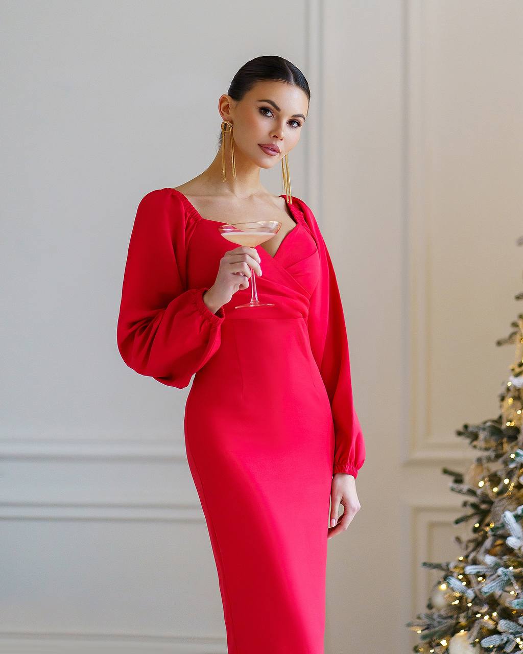 Woman in a red dress holding a glass in a festive setting with a Christmas tree.