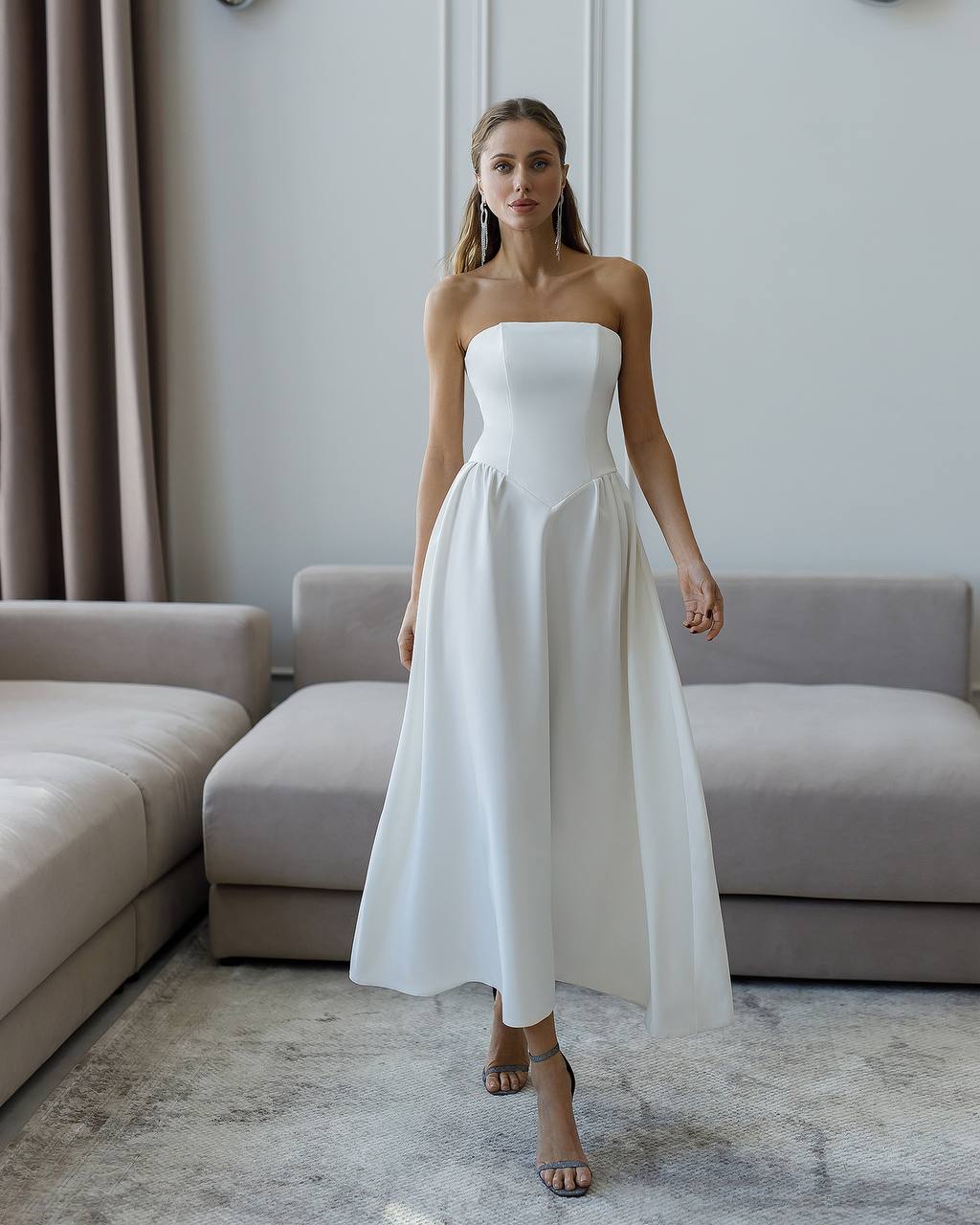 Woman wearing a strapless white dress in a living room setting