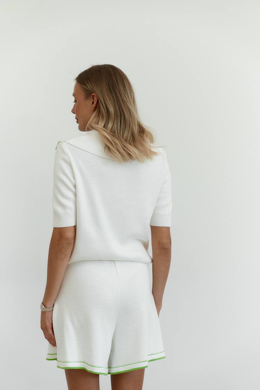 Woman wearing a white outfit with green trim on a plain background