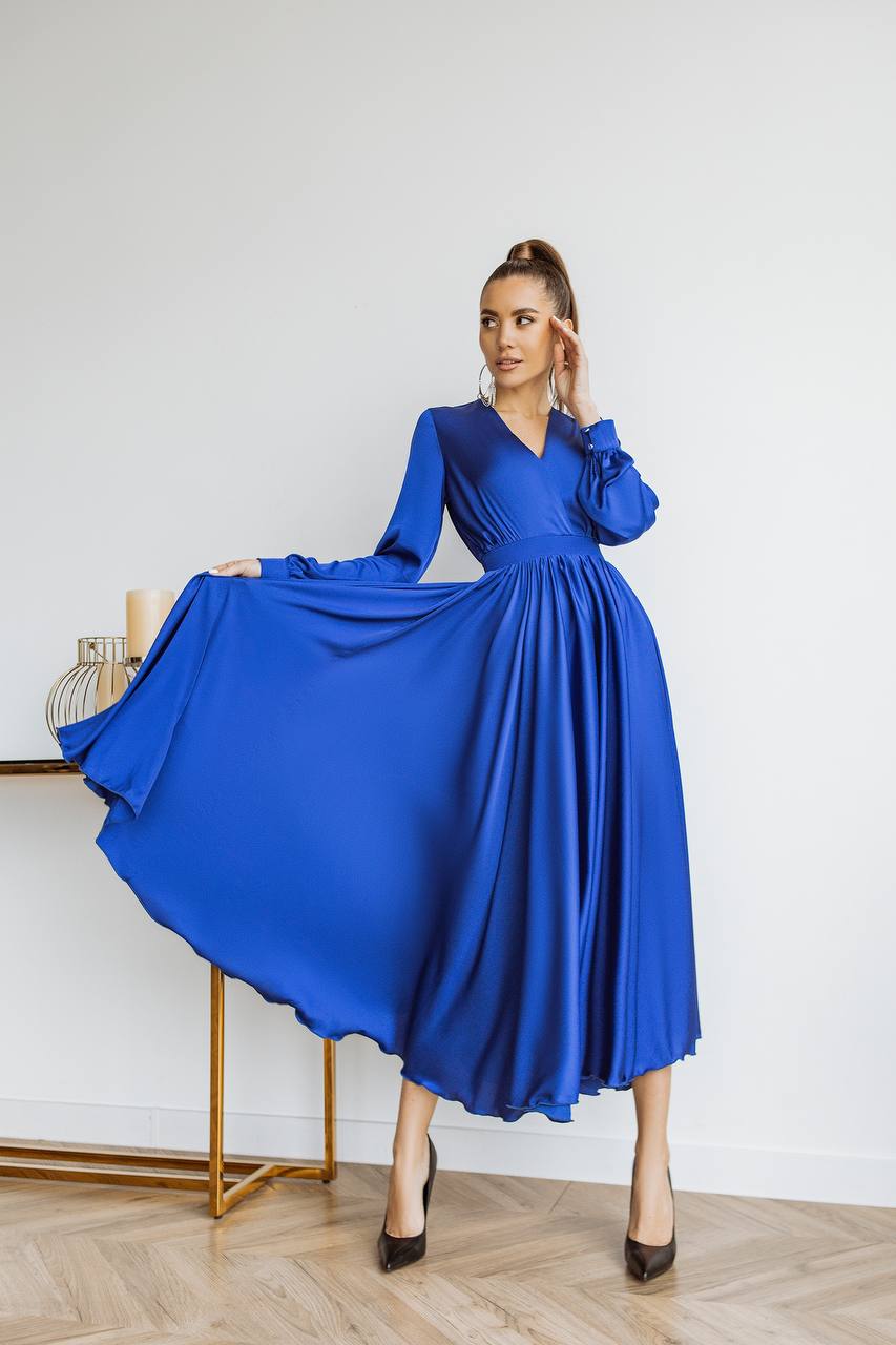 Woman wearing a blue dress in a room with a white wall and wooden floor.