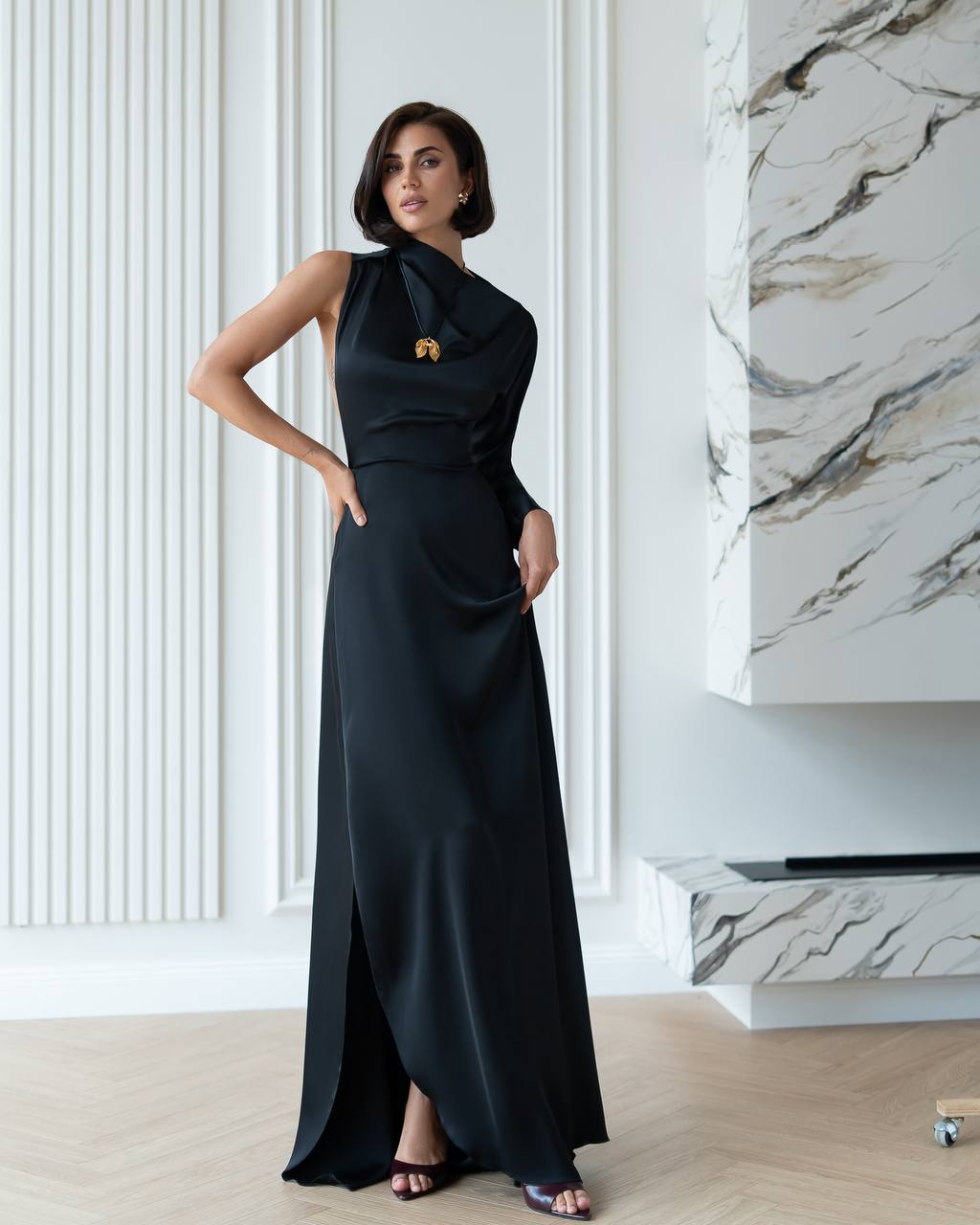 Woman in a black evening gown standing in an elegant interior setting.