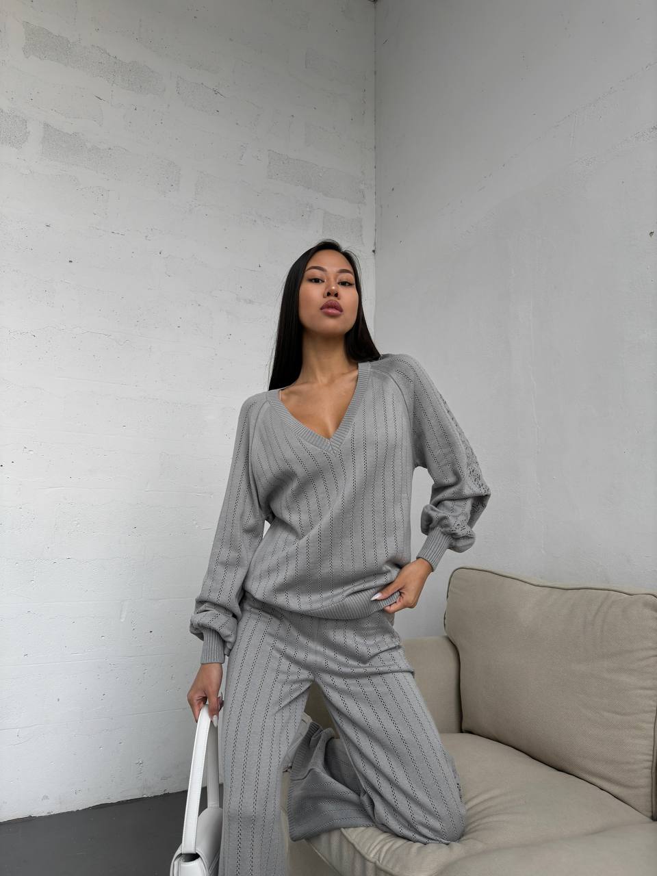 Woman in a gray ribbed loungewear set standing in a minimalistic room with a white wall and beige sofa.