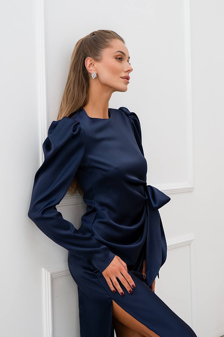 Woman wearing a navy blue dress with long sleeves against a white wall.