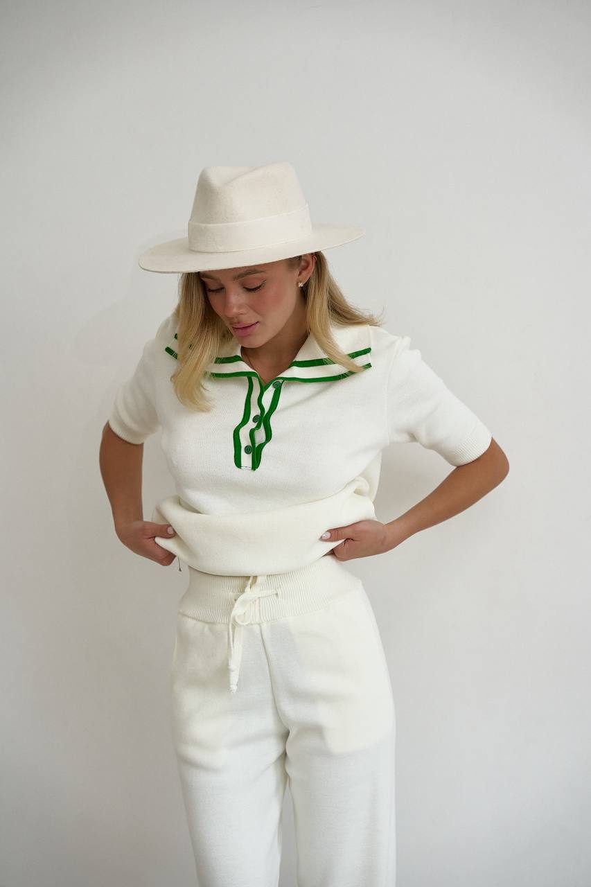 Woman wearing a white outfit with green accents and a white hat against a plain background
