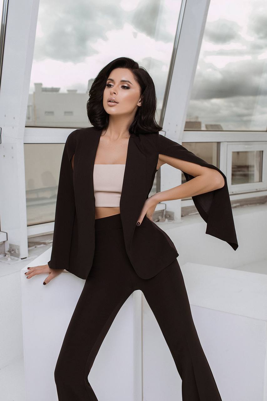 Woman in a black suit and beige top standing on a rooftop with cityscape background