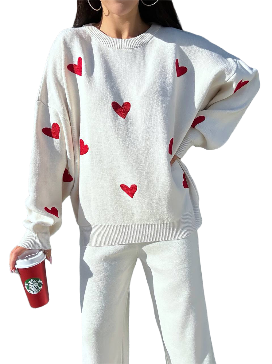 White sweater with red heart patterns worn by a person, holding a Starbucks cup.