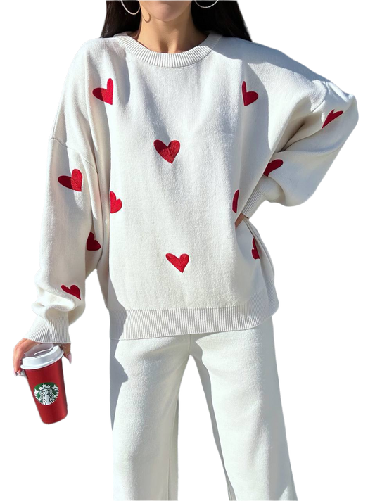 White sweater with red heart patterns worn by a person, holding a Starbucks cup.
