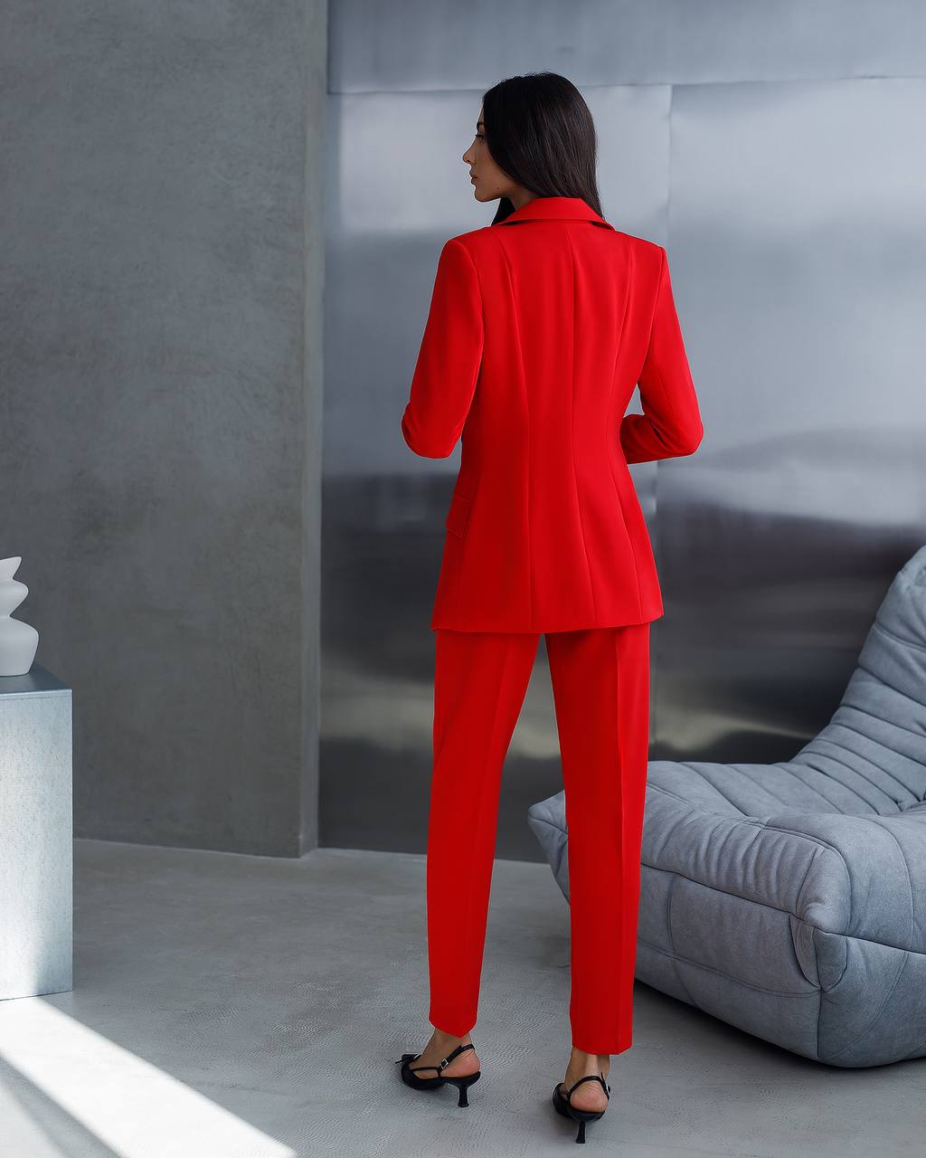 Woman in a red suit standing in a modern room with gray walls and furniture.