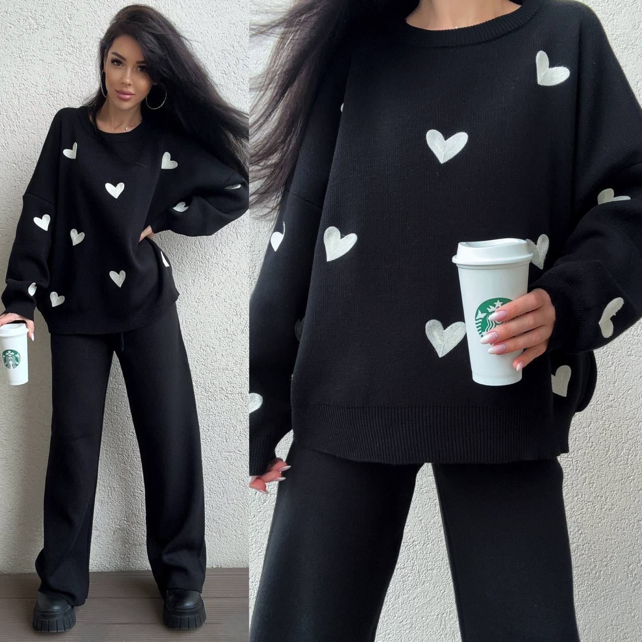 Person wearing a black sweater with white heart patterns, holding a Starbucks cup.