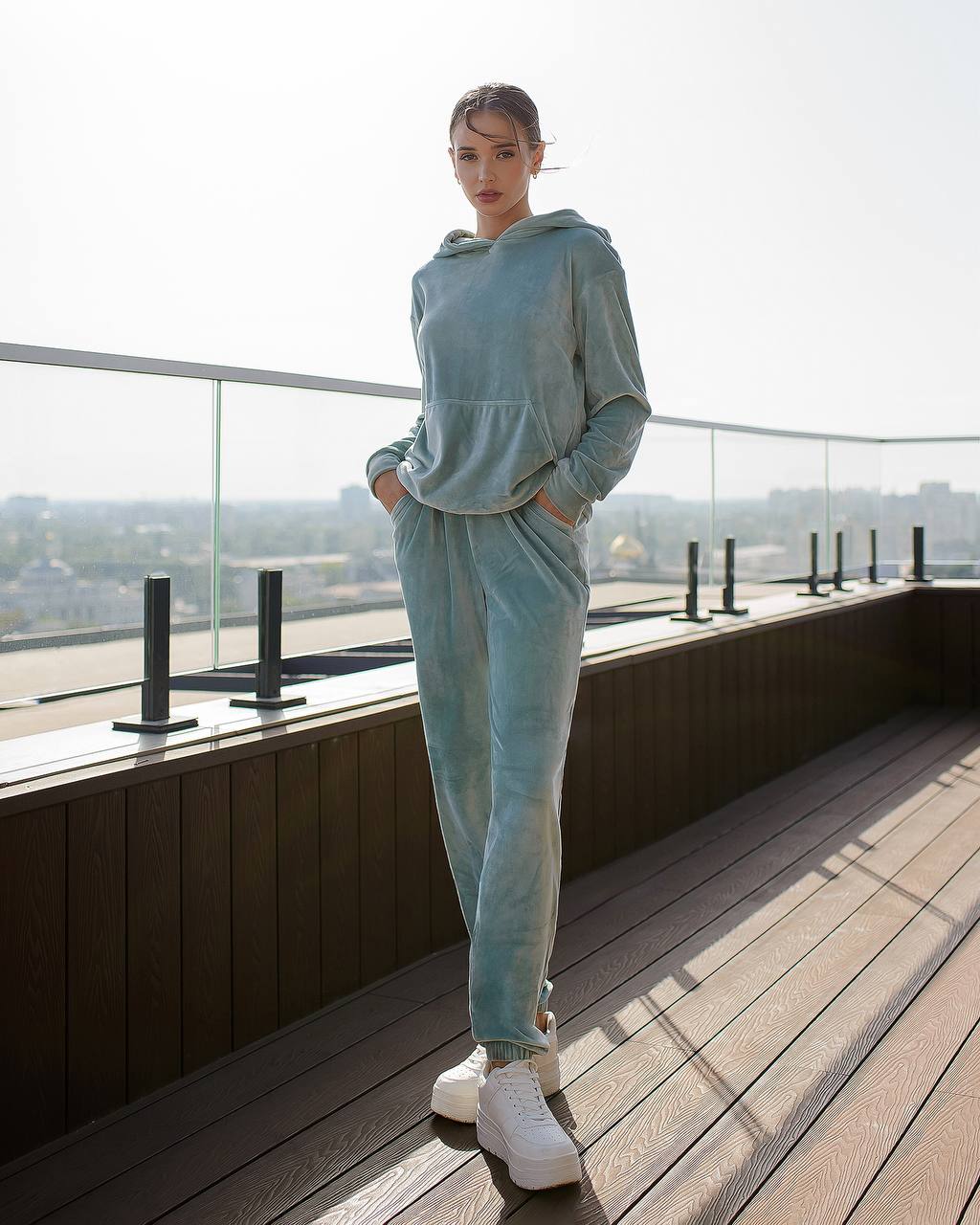 Person wearing a light blue tracksuit on a rooftop with a cityscape view.