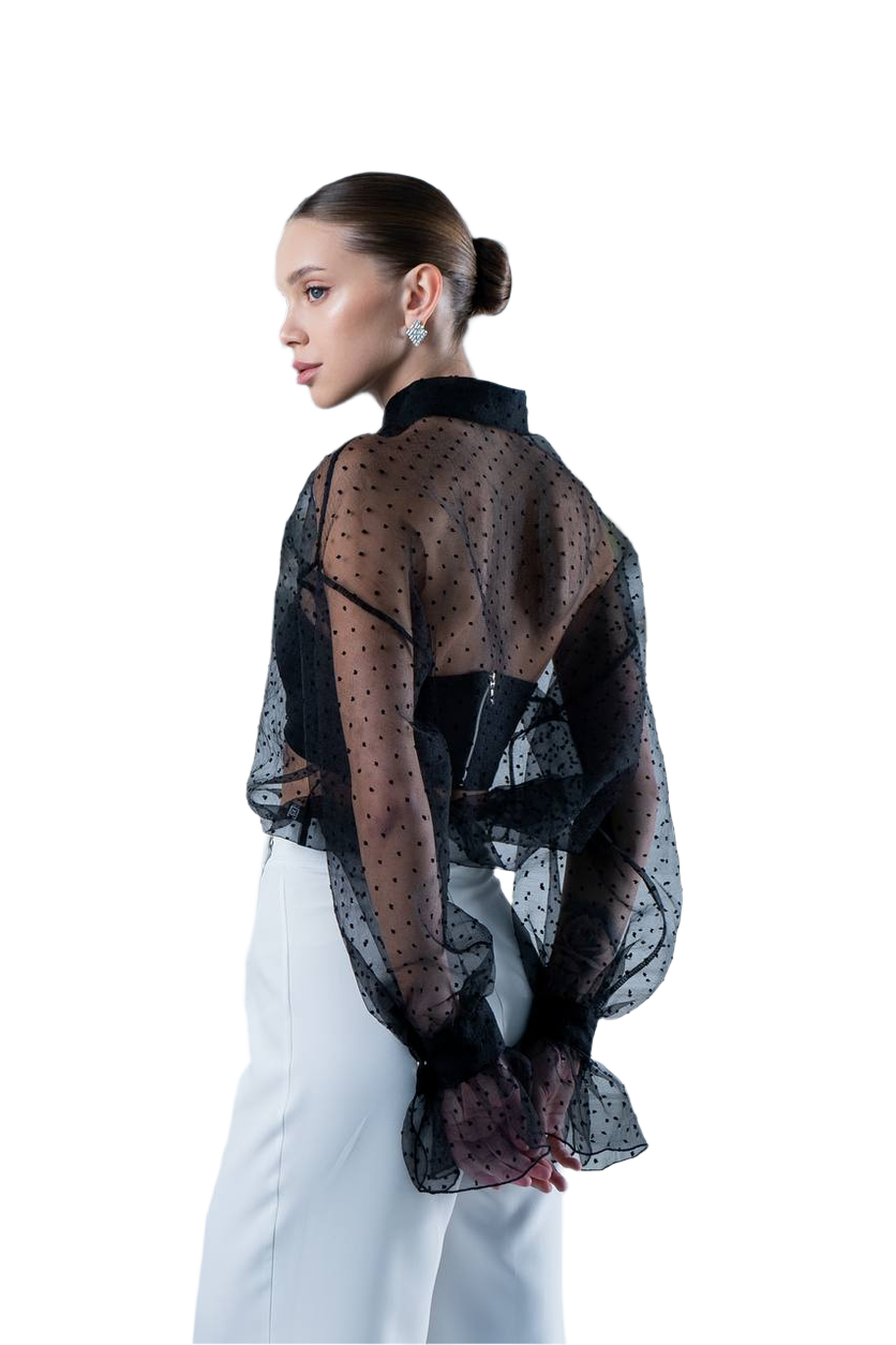 Woman wearing a sheer black polka dot blouse over a white dress on a white background