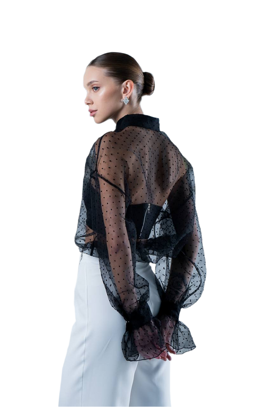 Woman wearing a sheer black polka dot blouse over a white dress on a white background