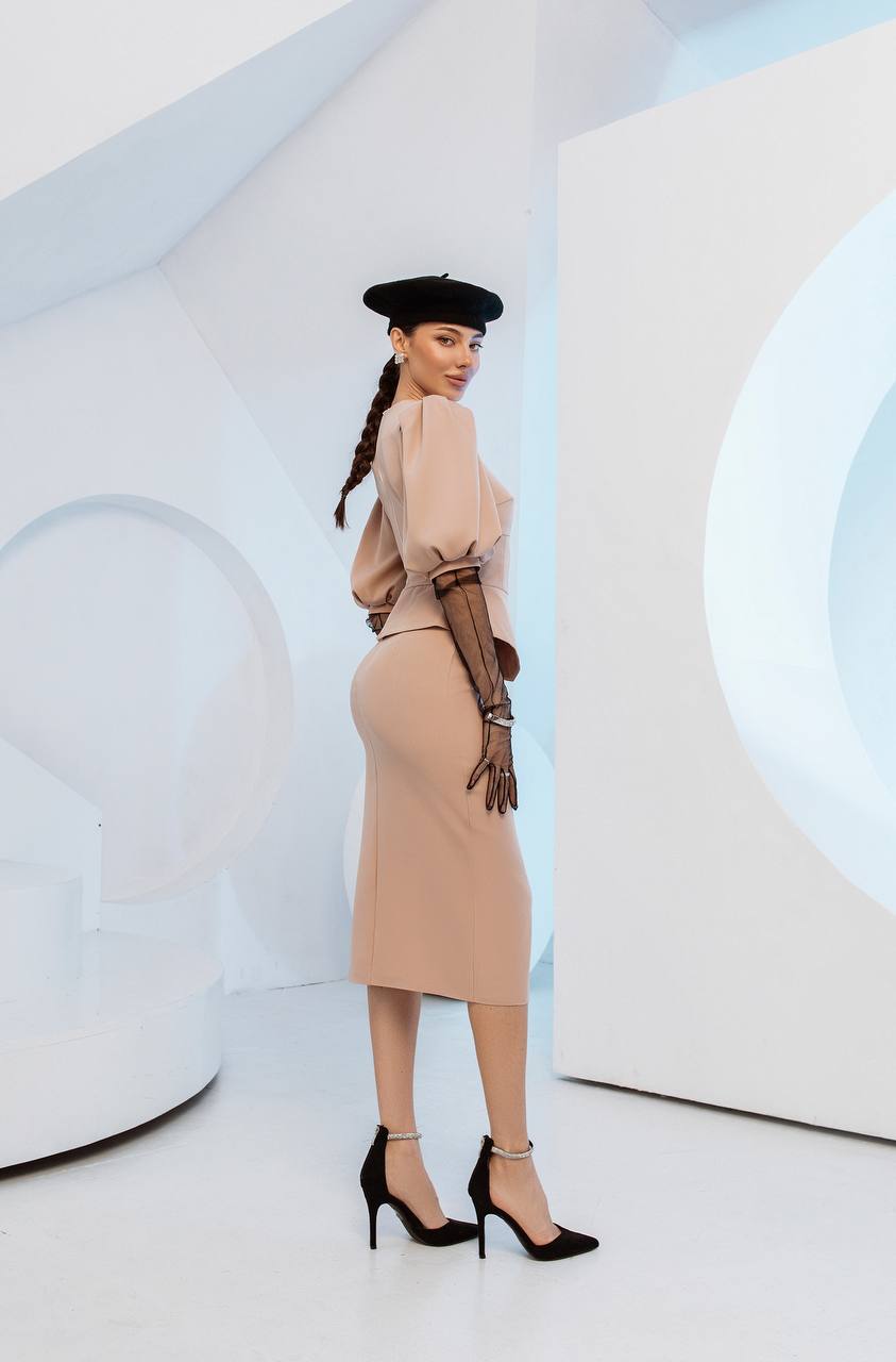 Woman in a stylish outfit with a beige sweater, skirt, and gloves against a modern white background.