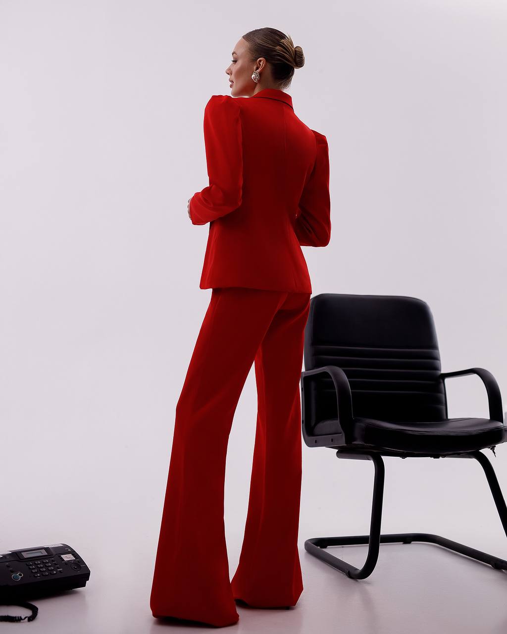 Person wearing a red suit standing next to a black chair on a white background