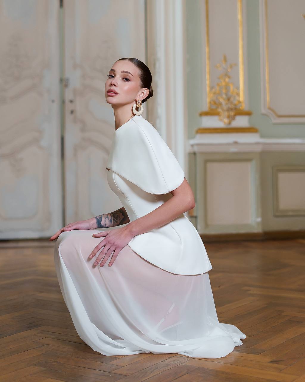 Woman in a white dress posing in an elegant room with gold accents.