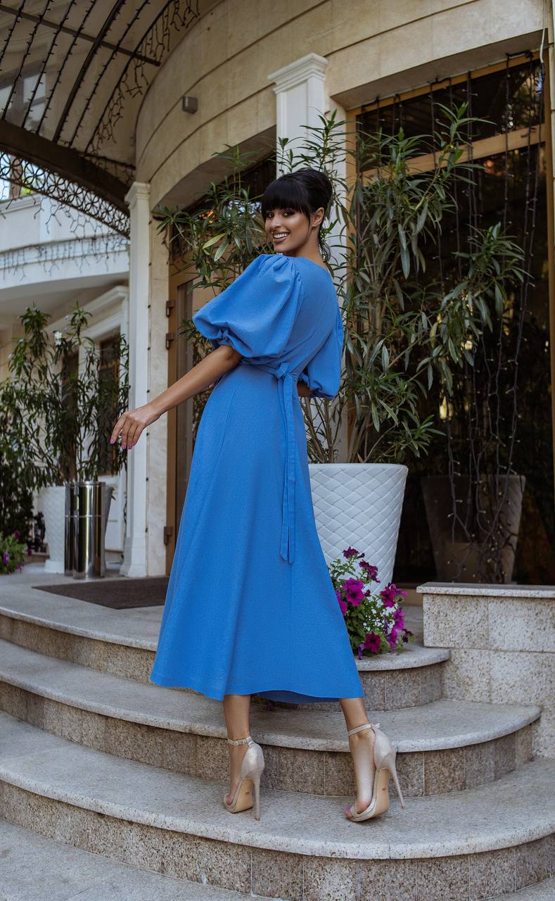 Woman in a blue dress standing on steps outdoors with plants and flowers in the background