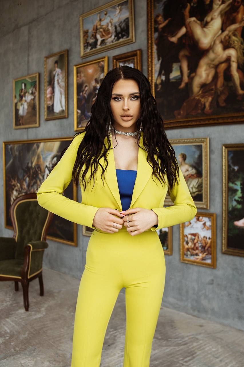 Woman in a yellow suit standing in an art gallery with classical paintings on the wall.