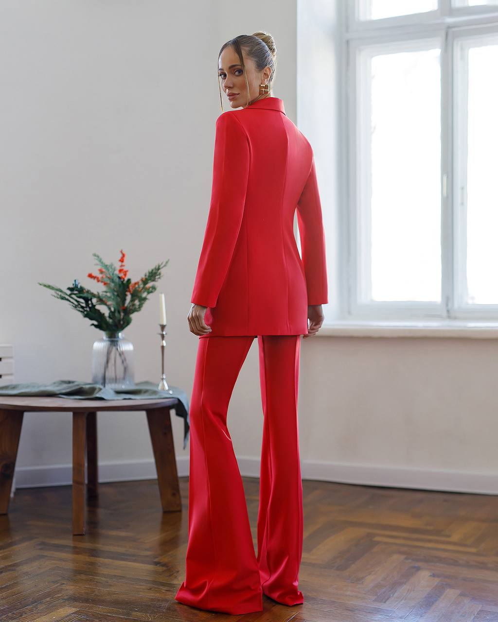 Person wearing a red suit standing in a room with a window and table.