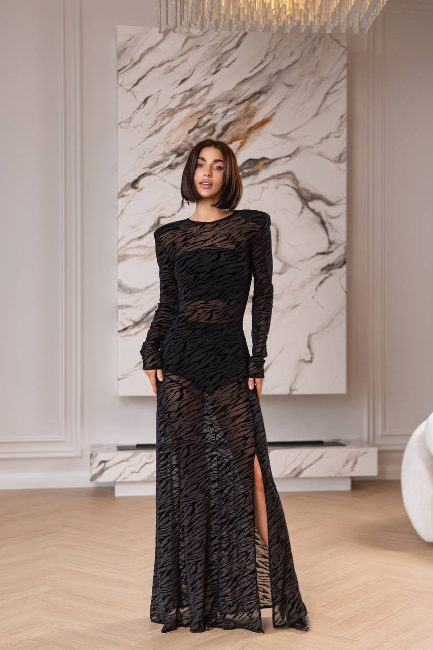 Woman in a black lace dress standing in a room with marble wall art.