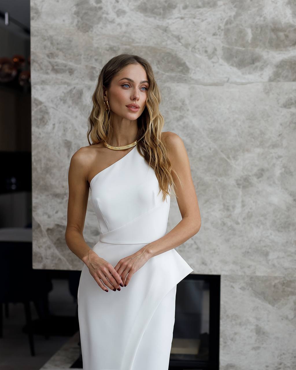 Woman wearing a white halter-neck dress against a textured wall.