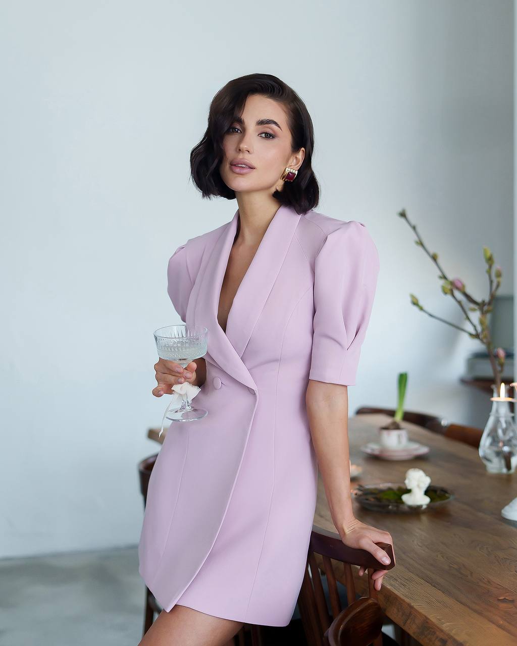 Woman in a light purple dress holding a glass of water in a modern interior setting.