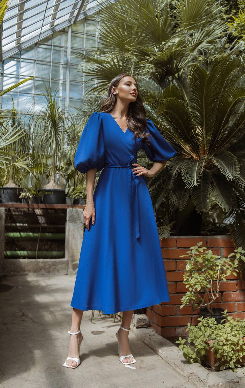 Woman in a blue dress standing in a greenhouse with plants around
