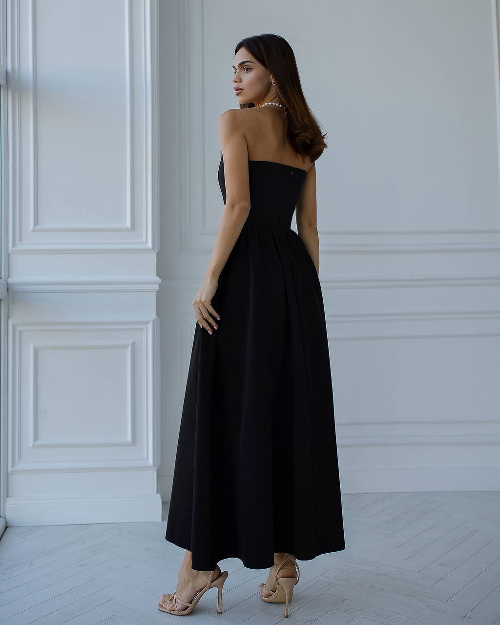 Woman wearing a black strapless dress in a white room