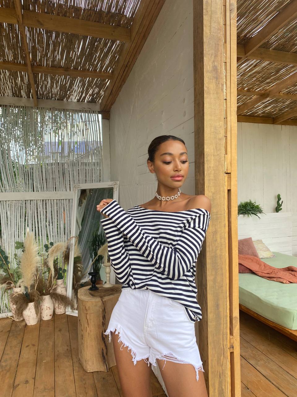 Woman wearing a black and white striped top and white shorts in a wooden interior setting.