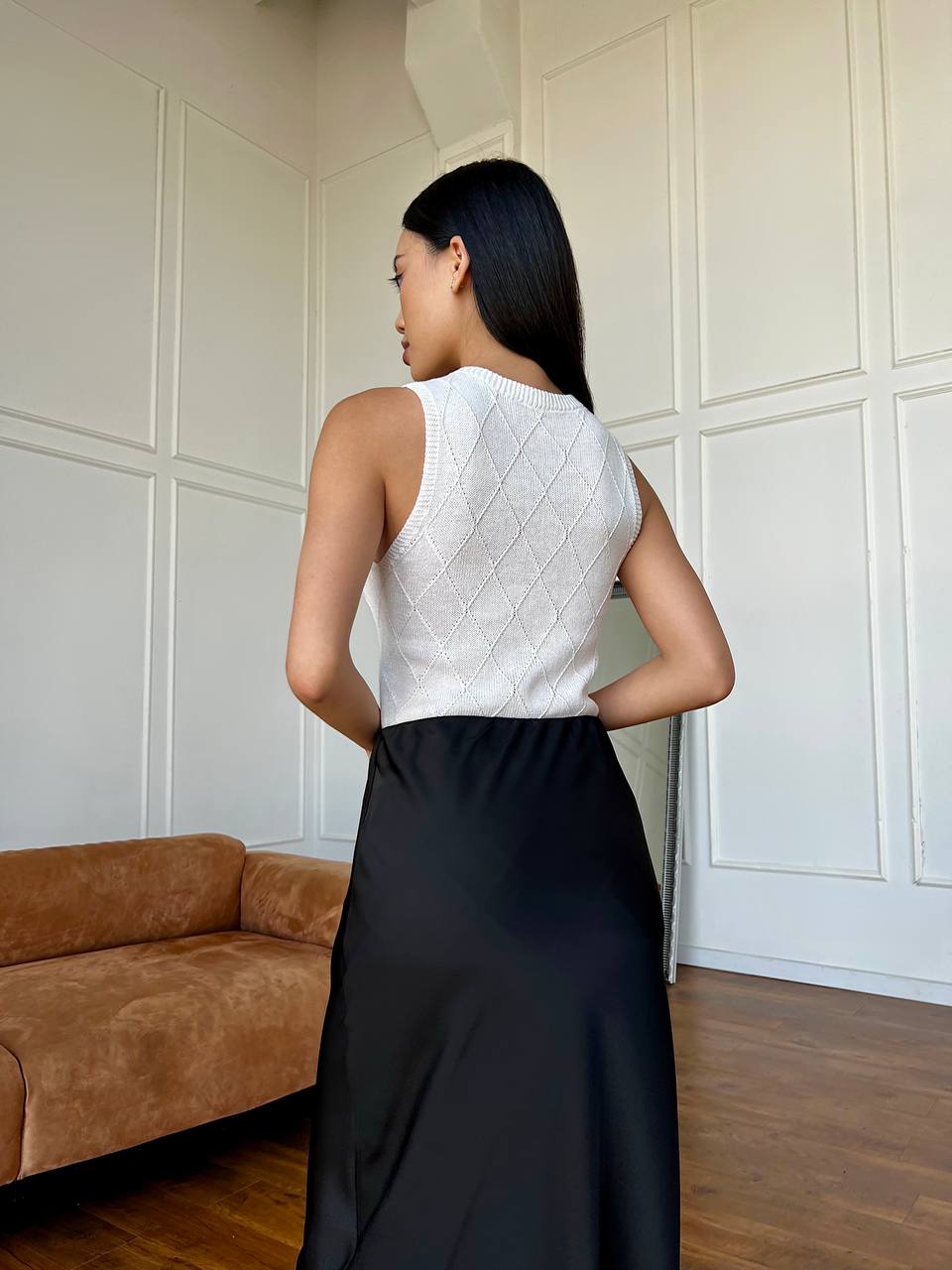 Woman wearing a white sleeveless top and black skirt in a room with a brown couch.