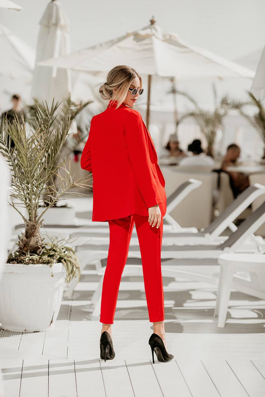 Woman in a red outfit standing on a sunlit deck with plants and people in the background