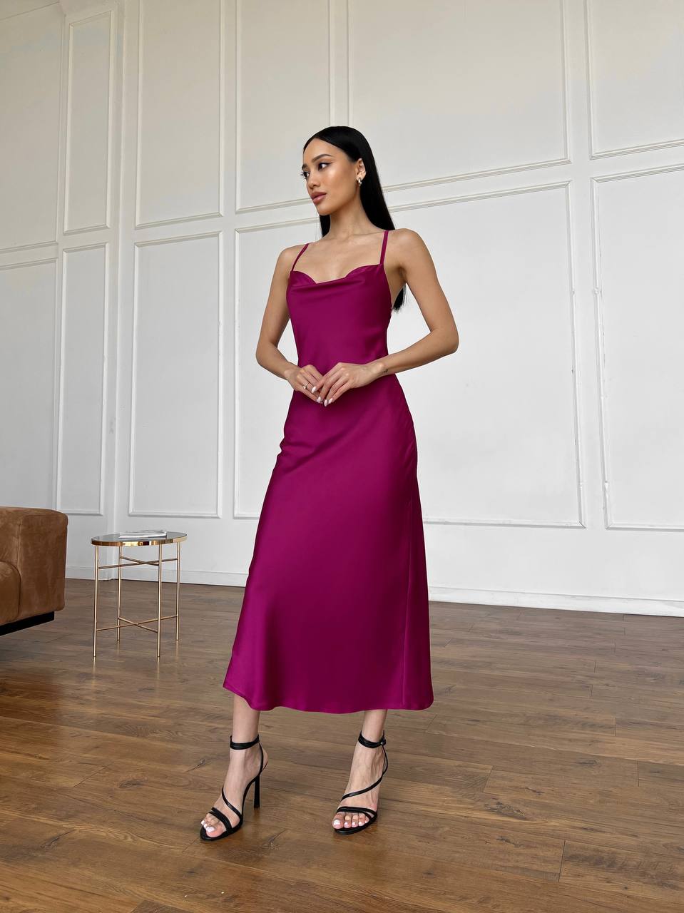 Woman wearing a magenta dress standing in a room with wooden flooring and white paneled walls.