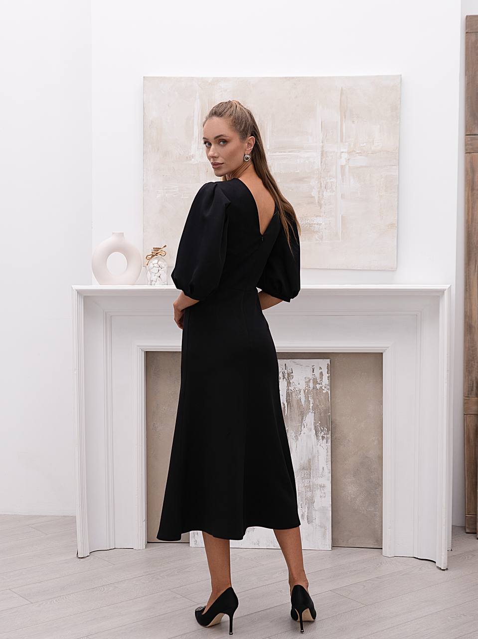 Woman wearing a black dress with a backless design in a minimalistic room.