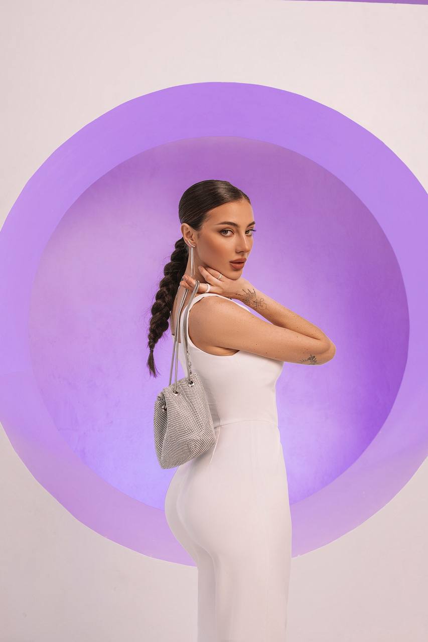Woman in a white dress holding a gray handbag against a purple circular background