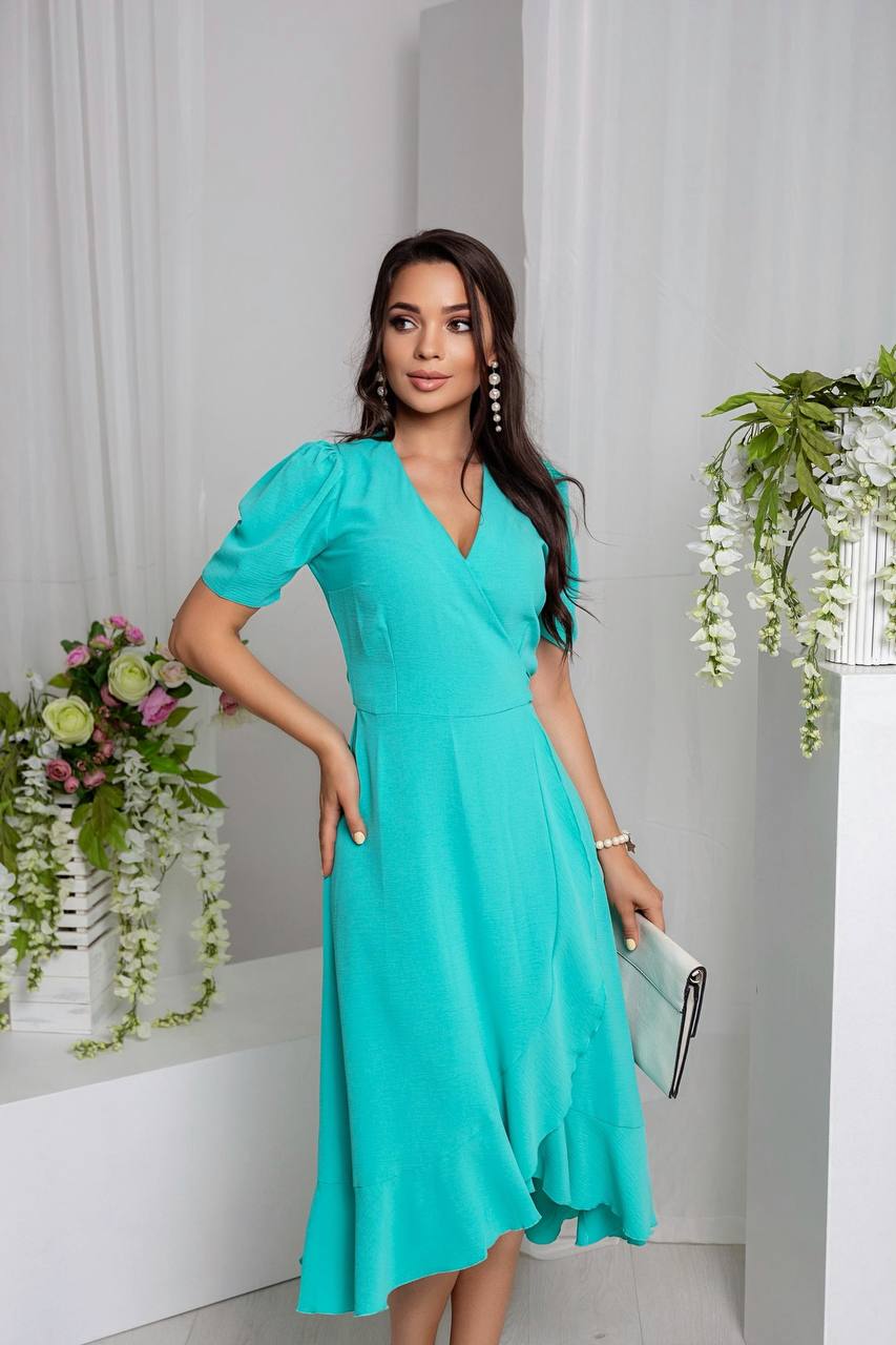 Woman in a turquoise dress standing in a room with white walls and green plants.