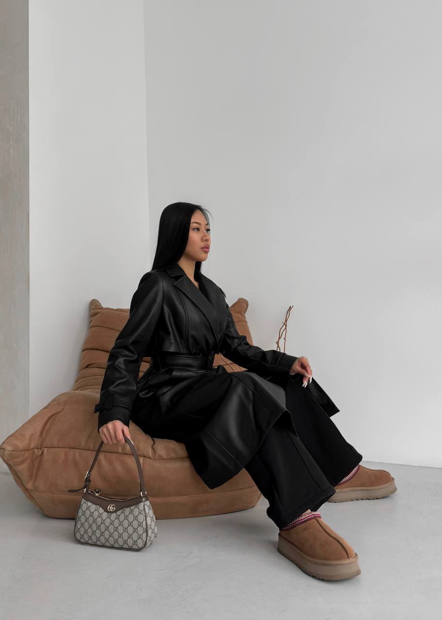 Woman in black outfit sitting on a brown couch with a handbag next to her.