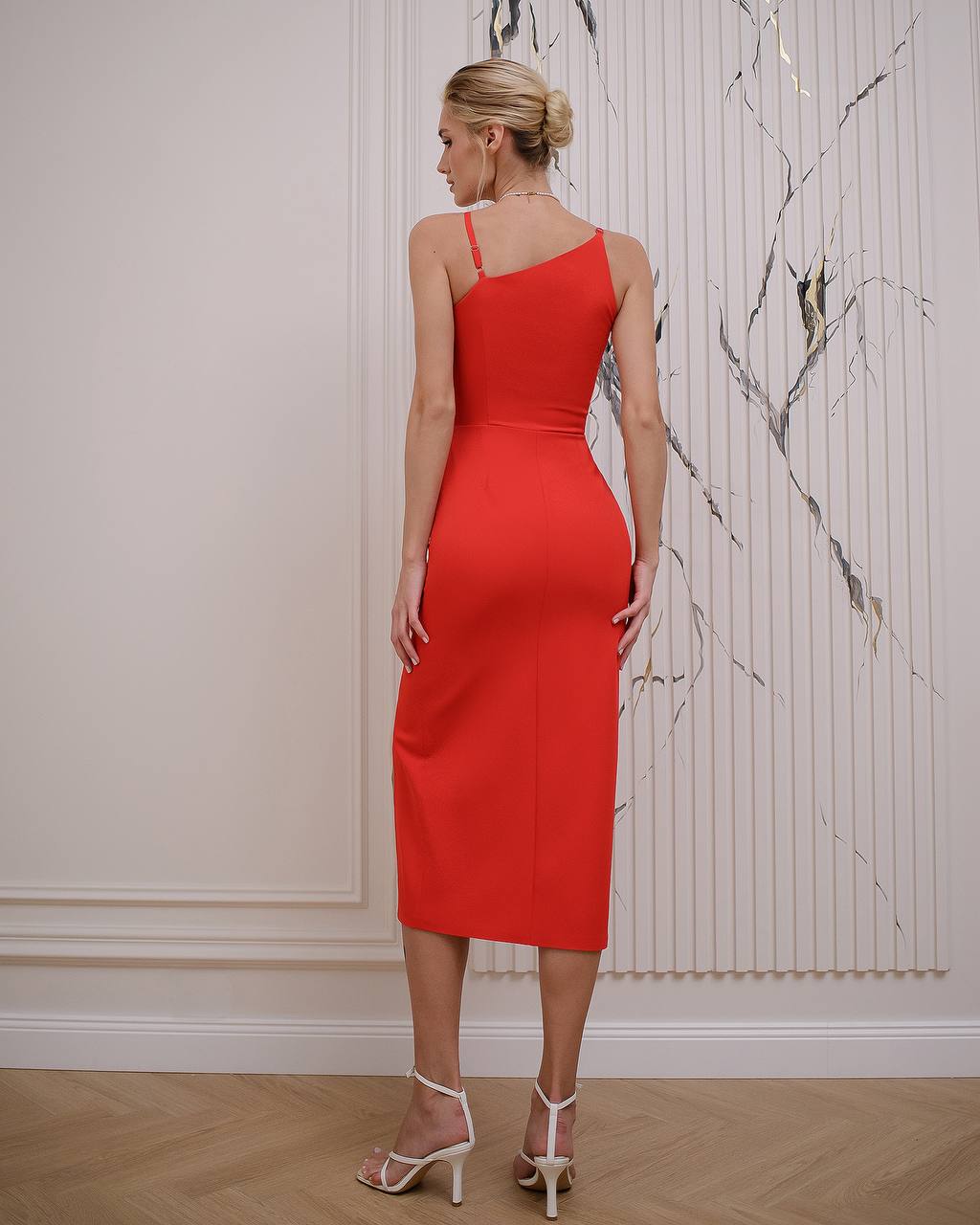 Woman wearing a red one-shoulder dress in an indoor setting with marble wall.