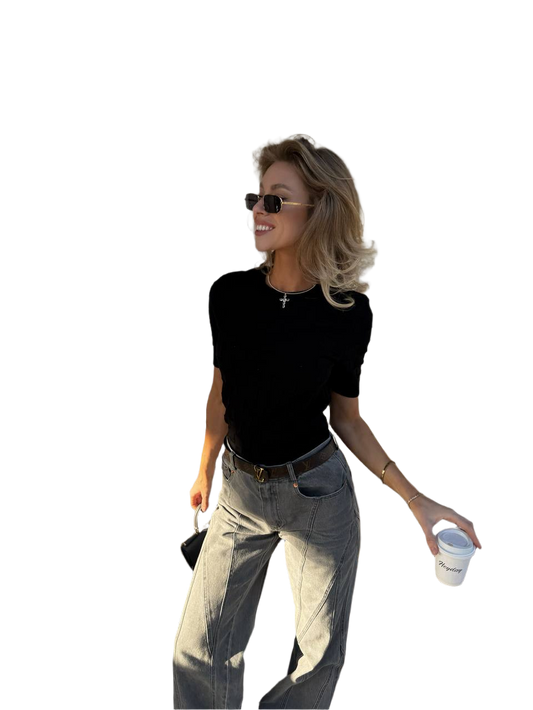 Woman wearing a black top and light-colored pants, holding a cup and a small bag on a white background
