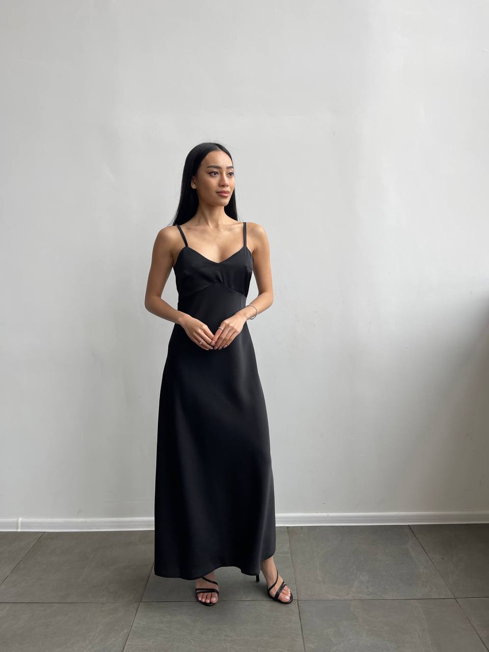 Woman wearing a black slip dress against a plain background