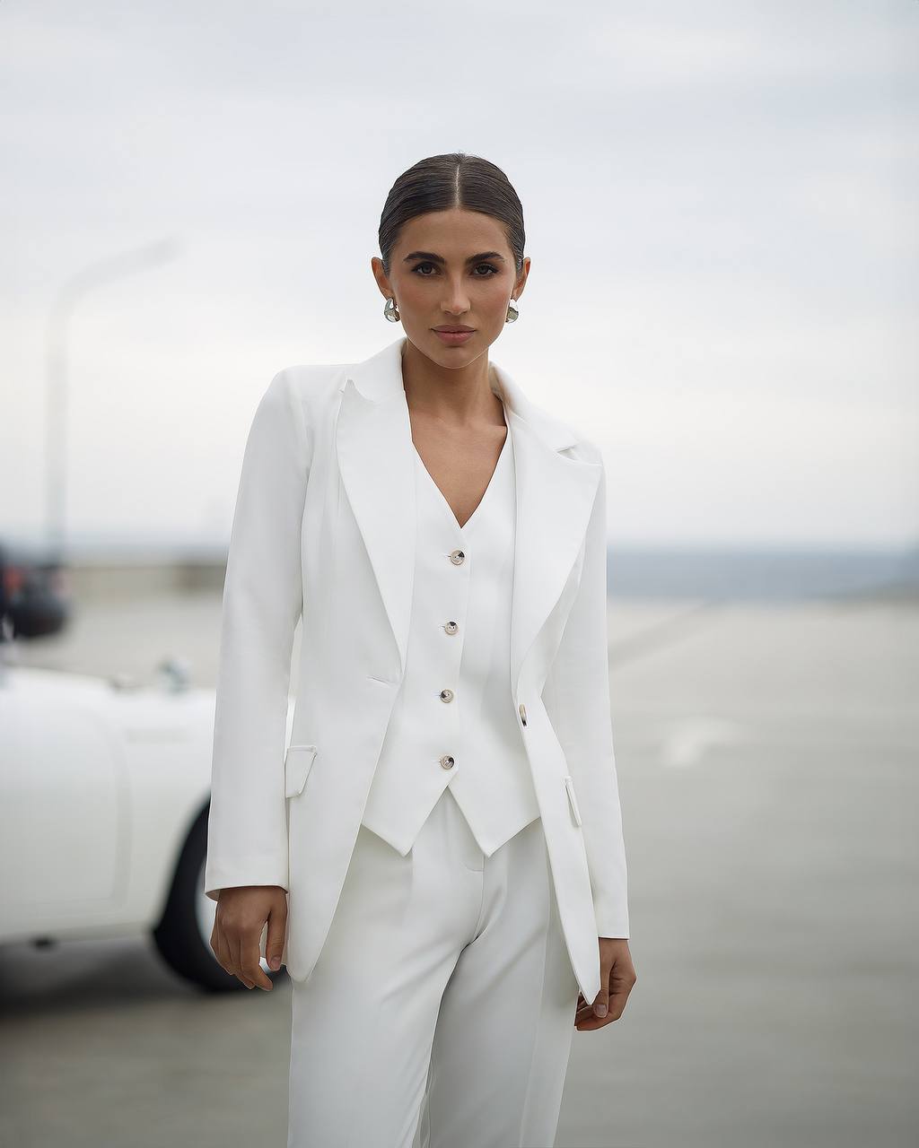 Woman wearing a white suit standing in a blurred indoor setting