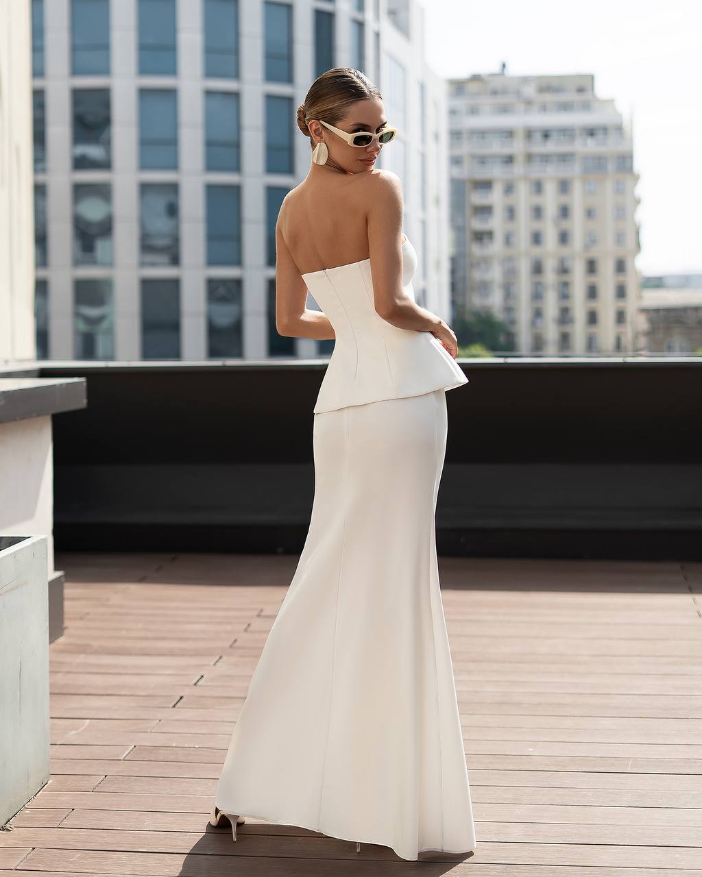 Woman in a white dress standing on a rooftop with cityscape background