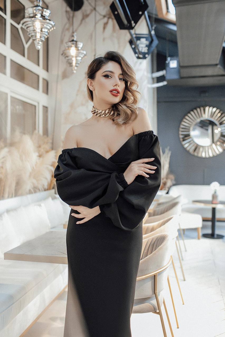 Woman in a black off-shoulder dress posing in an elegant interior setting.